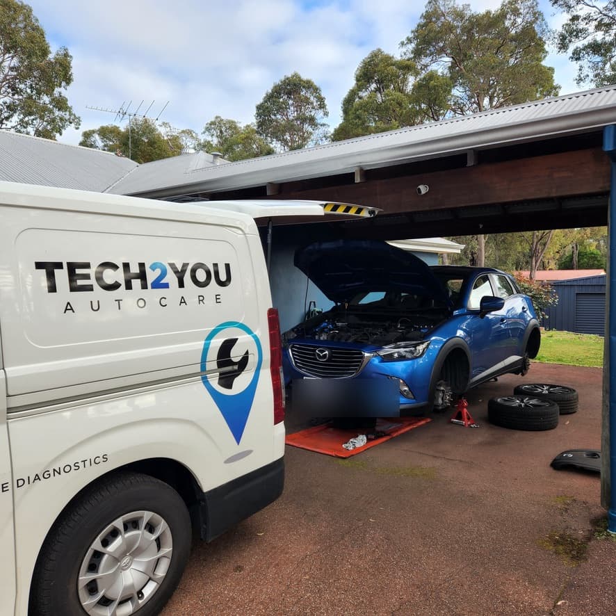 Tech2You van parked at a customer's driveway with the technician servicing a blue Mazda on-site